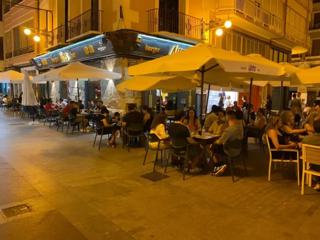 Terraza de Aires Grill Bar Elche con mesas y sombrillas por la noche