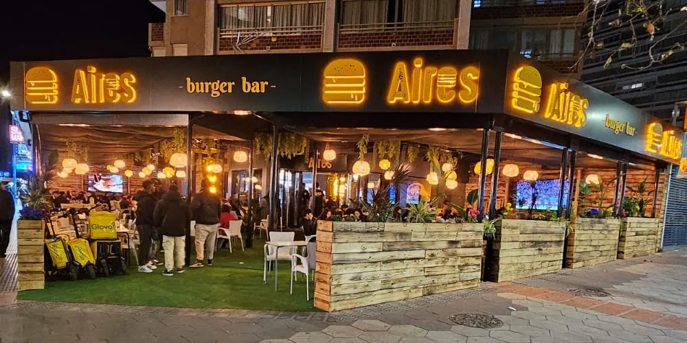Terraza de Aires Burger Bar Benidorm con mesas junto al rótulo iluminado