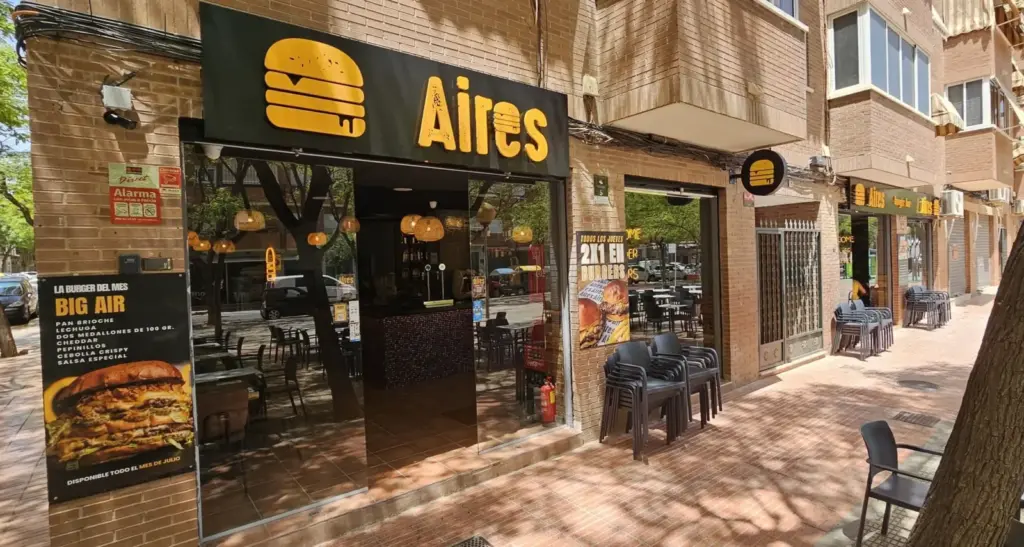 Fachada de Aires Burger Bar San Vicente del Raspeig con rótulo amarillo y mesas exteriores