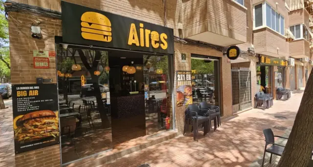 Fachada de Aires Burger Bar San Vicente del Raspeig con rótulo amarillo y mesas exteriores