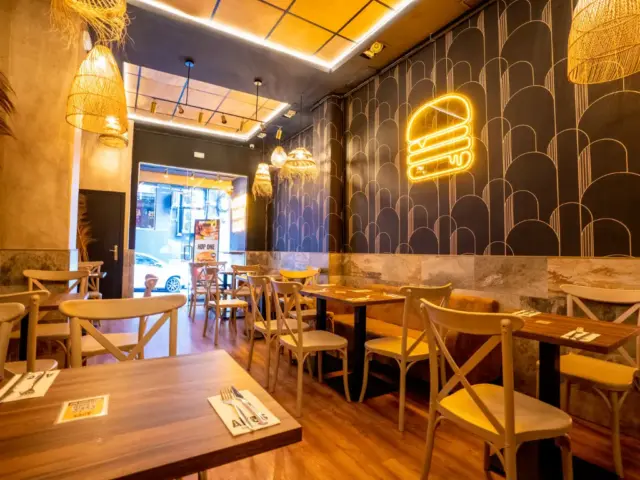 Interior de Aires Burger Bar Alicante con mesas de madera y un neón de hamburguesa
