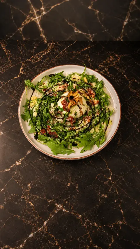 Burrata de la casa con hojas verdes y aliño vista desde arriba