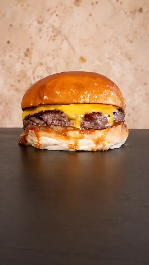 Hamburguesa Cheese Burger con queso fundido sobre fondo oscuro