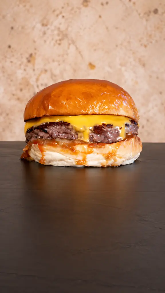 Hamburguesa Cheese Burger con queso fundido sobre fondo oscuro