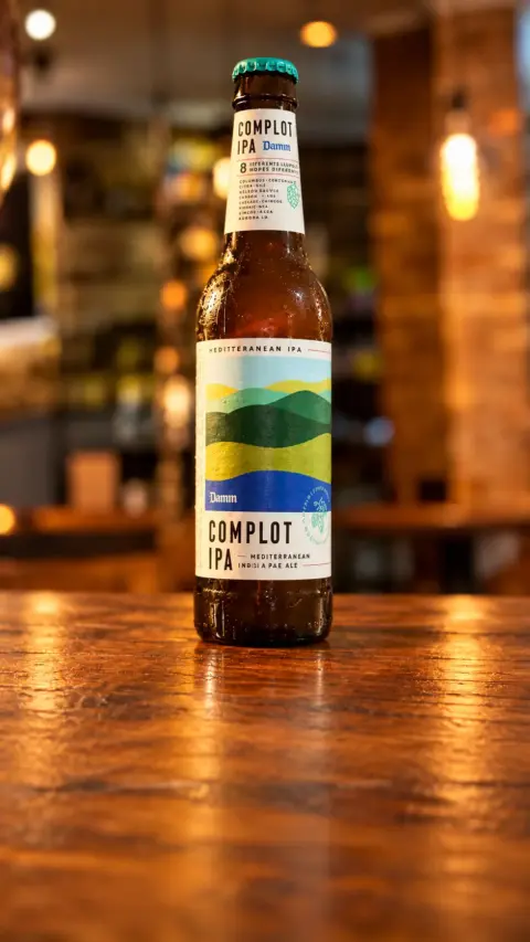 Botella de cerveza Complot IPA sostenida en la mano