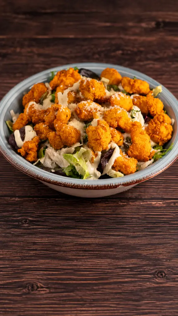 Ensalada César con trozos de pollo rebozado sobre hojas verdes