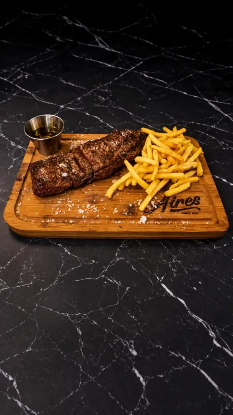 Entraña a las brasas con patatas fritas sobre una tabla de madera
