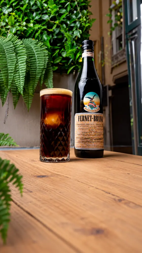 Vaso de Fernet con cola y botella de Fernet Branca sobre una mesa