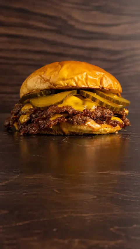 Flex Burger con queso y pepinillos sobre fondo oscuro