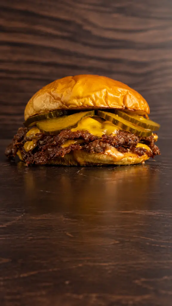 Flex Burger con queso y pepinillos sobre fondo oscuro