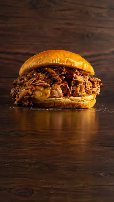 Hamburguesa La Pendeja con carne deshilachada sobre fondo oscuro