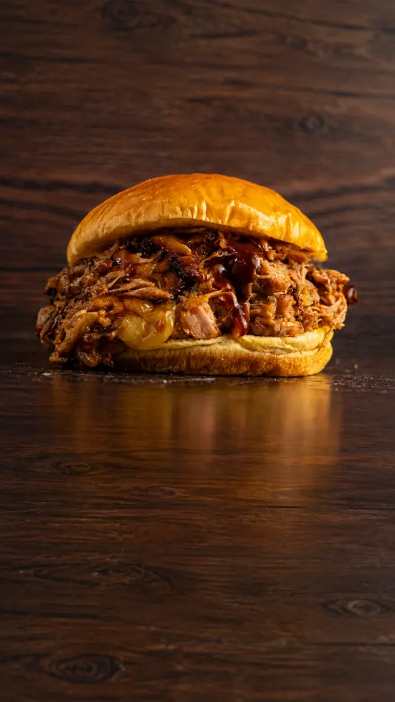 Hamburguesa La Pendeja con carne deshilachada sobre fondo oscuro