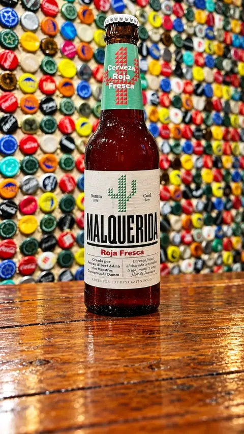 Botella de cerveza Malquerida sobre un fondo de chapas