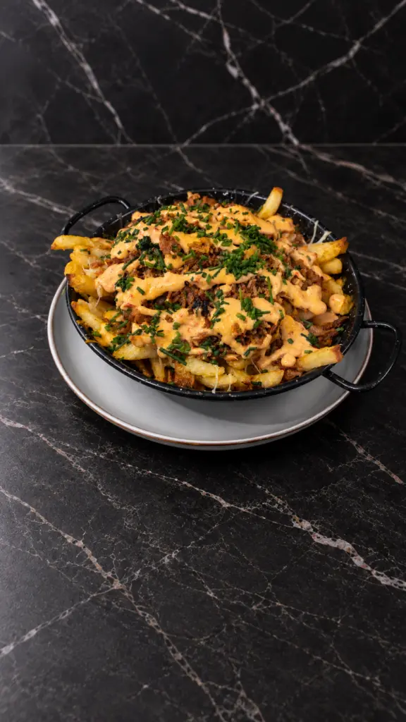 Patatas con carne deshilachada, salsa y hierbas en una cazuela