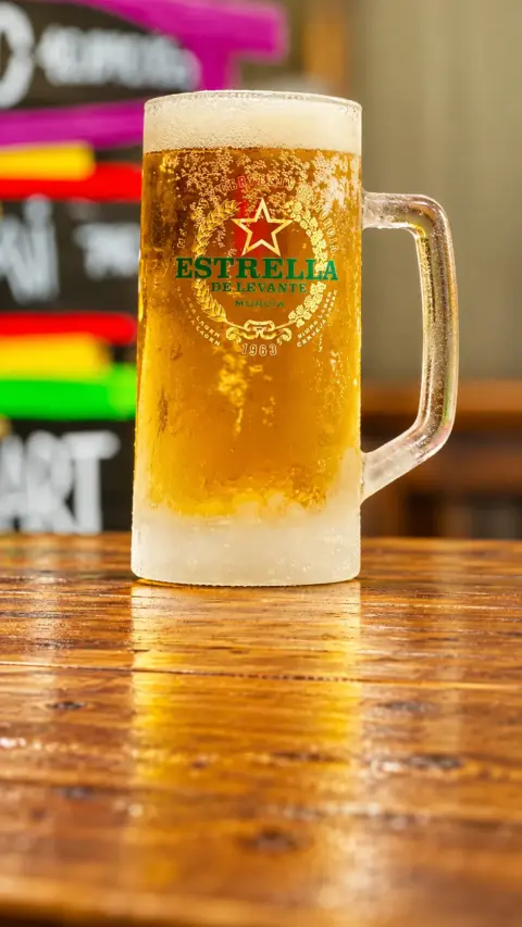 Jarra de cerveza Estrella de Levante sostenida junto a la barra